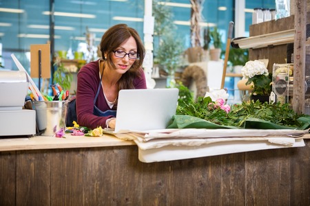 43661138 - mid adult female florist using laptop at counter in flower shop